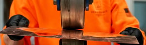 man using roller to shape a sheet of copper